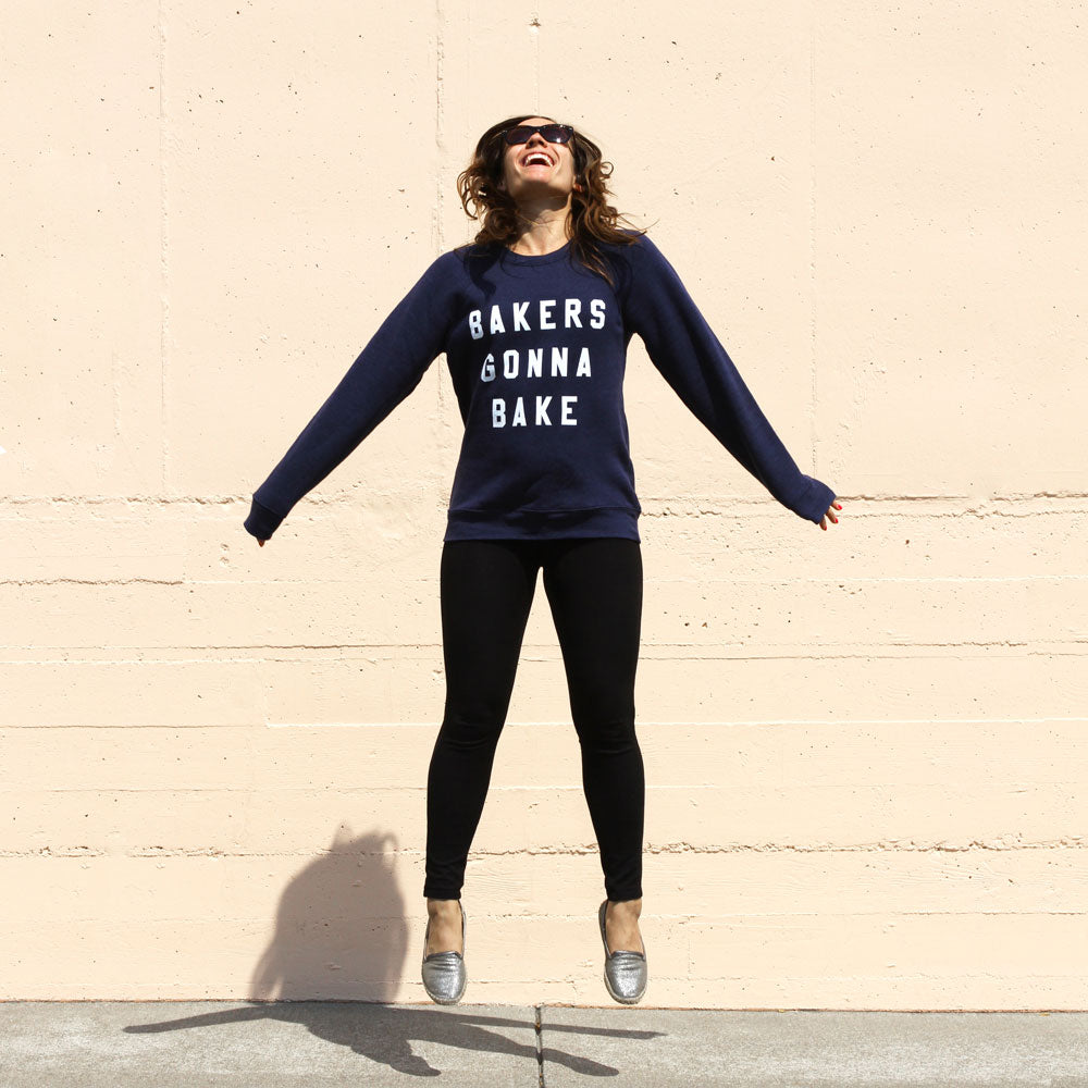 A woman jumping wearing Miss Jones Baking Co.- Bakers Gonna Bake Crewneck Navy sweatshirt