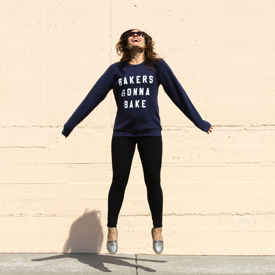 A woman jumping wearing Miss Jones Baking Co.- Bakers Gonna Bake Crewneck Navy sweatshirt